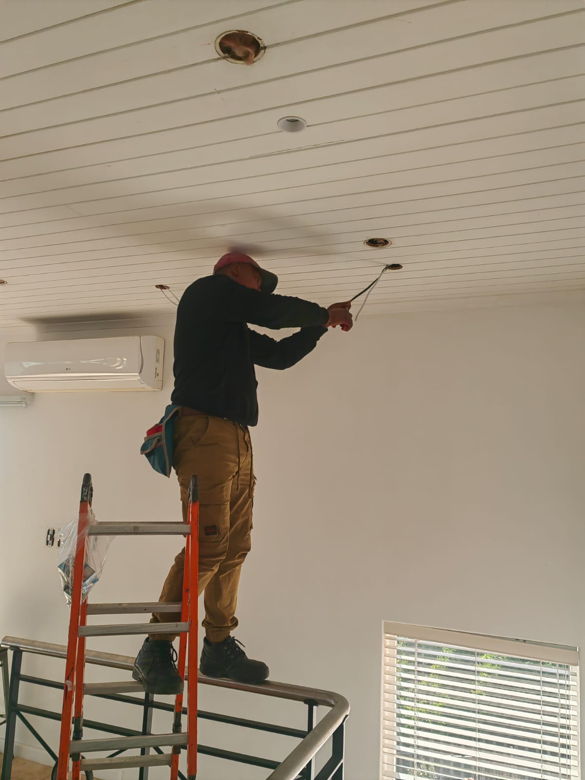 Electrician connecting wiring for a downlight fitting on a ladder